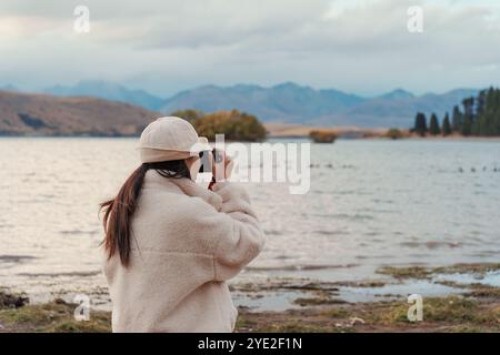 Vue arrière de la touriste profitant et prenant une photo avec un appareil photo compact sur le lac Tekapo en automne à la Nouvelle-Zélande Banque D'Images