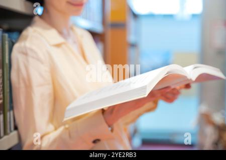 Méconnaissable jeune lisant un livre dans la bibliothèque, debout à côté d'une étagère. Banque D'Images