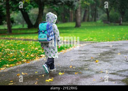 Un enfant en imperméable avec un sac d'école va à l'école sous la pluie. Banque D'Images