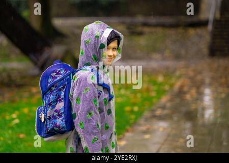 Un enfant en imperméable avec un sac d'école va à l'école sous la pluie. Banque D'Images