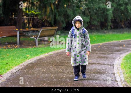 Un enfant en imperméable avec un sac d'école va à l'école sous la pluie. Banque D'Images