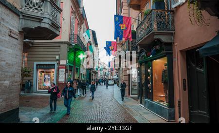 Une rue animée à Alba Italie ornée de drapeaux colorés. Les gens se promènent à travers le sentier pavé, en profitant des boutiques locales et de l'atmosphère animée Banque D'Images