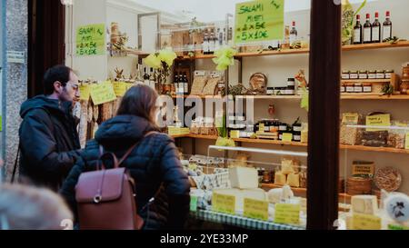 Un couple parcourt une boutique artisanale à Alba, en Italie, captivée par une variété de salami, fromages locaux et spécialités maison exposées, mettant en valeur le Banque D'Images