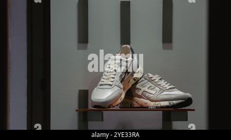 Une paire de baskets élégantes est présentée sur une étagère en bois élégante à l'intérieur d'un magasin à la mode à Alba, en Italie. La lumière de l'après-midi met en valeur leur design Banque D'Images