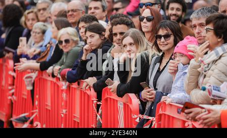 Un groupe diversifié de spectateurs se réunit derrière des barrières, immergés dans l'anticipation lors d'un événement local à Alba, en Italie, mettant en valeur l'atmosphère animée de t Banque D'Images