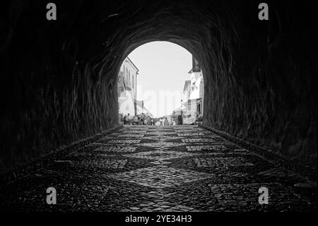 Vue monochrome du tunnel menant à une rue ensoleillée d'Albufeira, mettant en valeur le célèbre travail pavé à motifs Banque D'Images