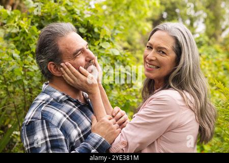 Couple mature souriant profitant d'un moment tendre ensemble dans un jardin luxuriant, à l'extérieur Banque D'Images