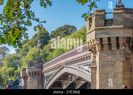 Gros plan sur un pont de pierre historique orné de ferronneries et de tours enjambent une rivière. Une ligne d'arbres sont en arrière-plan et un ciel clair est au-dessus. Banque D'Images