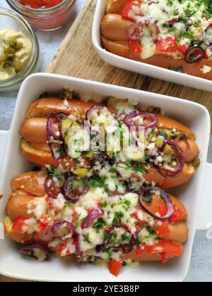 Hot Dogs cuits au four avec fromage fondu, oignons rouges, tomates et cornichons dans un plat de cuisson Banque D'Images