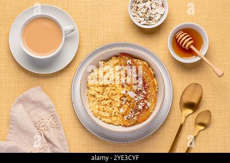 Photographie alimentaire de bouillie de millet avec banane caramélisée, noix de pécan, noix, flocons de noix de coco, chia, graines de lin, miel, thé au lait d'amande Banque D'Images