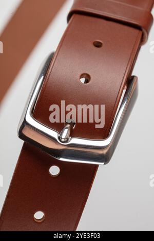 Partie d'une ceinture classique en cuir marron clair avec une boucle sur un fond gris. Banque D'Images