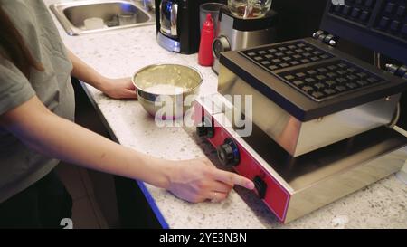 La cuisine d'un petit café confortable. Une jeune fille cuisinière prépare les légumes verts et les tomates et termine la cuisson du plat fini. Banque D'Images