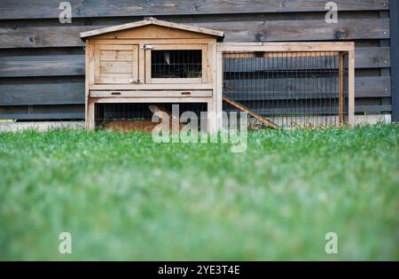 Une huche à lapins en bois de deux étages avec une enclos pour animaux et deux lapins couchés à l'intérieur se tient sur l'herbe dans le jardin près d'une clôture en bois. PET br Banque D'Images