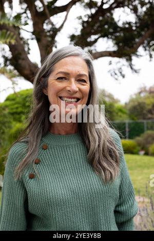 Femme mature souriante profitant du jardin extérieur dans un pull vert confortable Banque D'Images