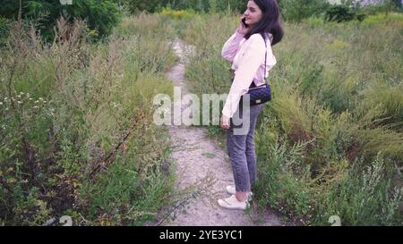 Explorant un sentier naturel, une jeune femme avec un sac noir sur ses épaules marche le long d'un chemin entouré de verdure lumineuse et de plantes sauvages. Parfait Banque D'Images