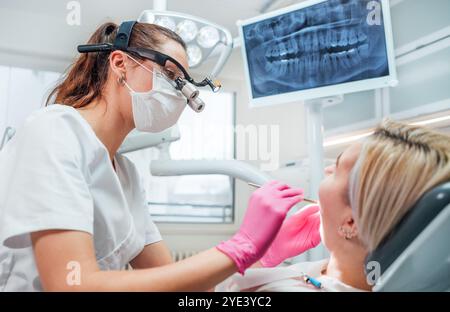 Dentiste femme médecin habillé uniforme dans des loupes effectuant des soins dentaires préventifs. Clinique dentaire visite d'un service médical moderne. Patien Banque D'Images