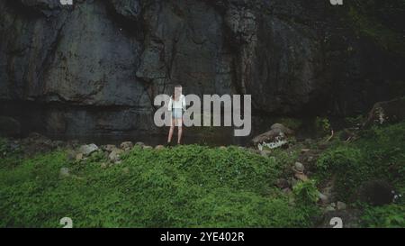 Jeune femme se tient seule, regardant une falaise de basalte massive dans une forêt tropicale luxuriante, perdue dans ses pensées lors d'une randonnée aventureuse à travers l'île de moorea en polynésie française Banque D'Images