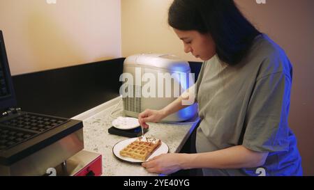 Il y a une gaufre préparée sur une assiette et un jeune cuisinier termine la préparation du plat fini. La cuisine d'un petit café confortable. Banque D'Images
