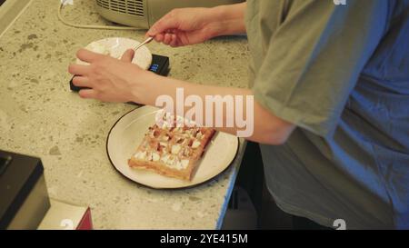 Il y a une gaufre préparée sur une assiette et un jeune cuisinier termine la préparation du plat fini. La cuisine d'un petit café confortable. Banque D'Images