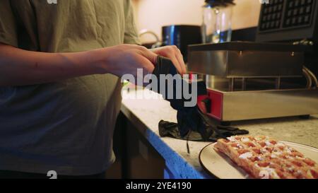 Il y a une gaufre préparée sur une assiette et un jeune cuisinier termine la préparation du plat fini. La cuisine d'un petit café confortable. Banque D'Images