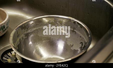 Gros plan des mains lavant un bol en acier inoxydable sous l'eau courante dans l'évier. L'accent est mis sur le processus de nettoyage et la cuisine quotidienne Banque D'Images