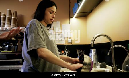 Dans la cuisine d'un petit café, une fille prépare des plats délicieux. Elle lave la vaisselle et prépare tous les outils. Banque D'Images