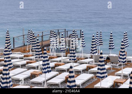 Parasols rayés bleus et blancs fermés et chaises longues vides sur la plage Promenade des Anglais, Nice, France, Côte d'Azur, Sud de la France Banque D'Images