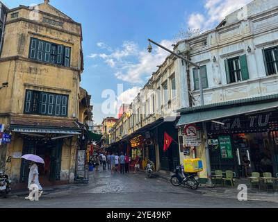 Hanoi, Vietnam : la vie quotidienne, la circulation et la skyline dans les rues bondées du centre de la capitale, avec des voitures et des motos qui passent à pleine vitesse Banque D'Images