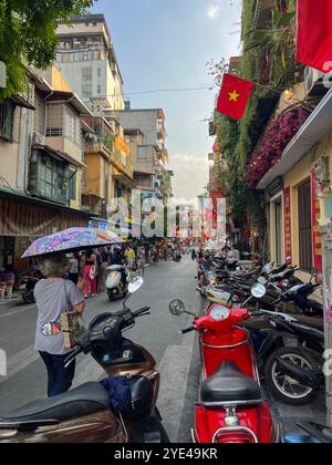 Hanoi, Vietnam : la vie quotidienne, la circulation et la skyline dans les rues bondées du centre de la capitale, avec des voitures et des motos qui passent à pleine vitesse Banque D'Images