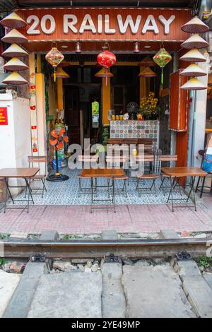 Vietnam : Hanoi train Street, étroite rocade qui voit les trains quotidiens passer à proximité des bâtiments de chaque côté des voies ferrées avec des gens buvant Banque D'Images