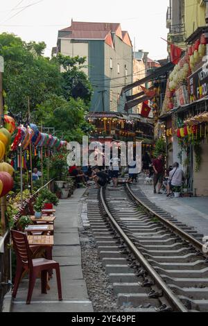 Vietnam : Hanoi train Street, étroite rocade qui voit les trains quotidiens passer à proximité des bâtiments de chaque côté des voies ferrées avec des gens buvant Banque D'Images