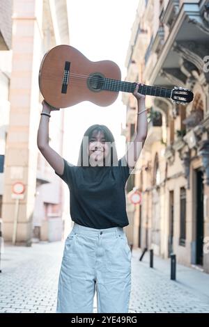 portrait vertical d'une jeune femme latine soulevant une guitare classique au-dessus de sa tête Banque D'Images