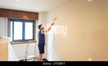 jeune barbu utilisant un rouleau à peinture sur un mur de sa chambre Banque D'Images