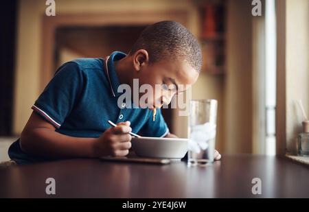 Enfant, garçon et manger des pâtes à la maison pour la nutrition, le développement affamé et sain à table. Enfant africain, nourriture et spaghetti repas dans la maison pour le déjeuner Banque D'Images