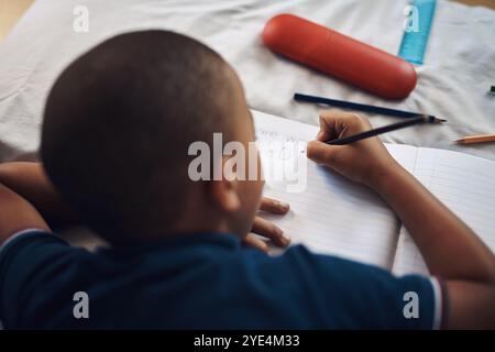 Garçon, couché et écrit avec un livre dans la chambre pour la créativité, la littérature ou le dessin pour l'activité éducative à la maison. Jeune, homme ou enfant Banque D'Images