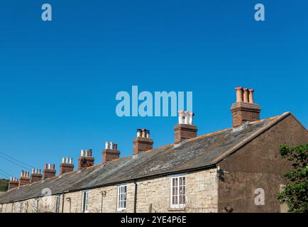 Niché le long de la côte accidentée de la baie de Kimmeridge, une rangée de charmantes chalets de pêcheurs se dresse fièrement sous un ciel bleu immaculé. Dorset, Royaume-Uni Banque D'Images