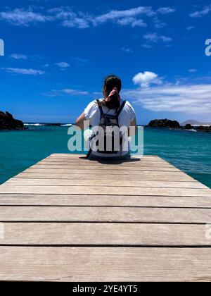 FILLE SUR SON DOS ASSISE SUR UNE PROMENADE EN BOIS REGARDANT LA MER Banque D'Images