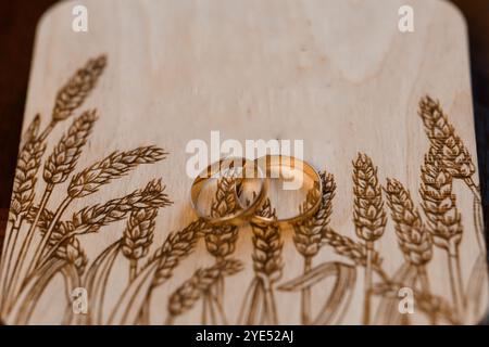 Anneaux de mariage élégants sur planche en bois soigneusement conçue avec motif de blé. Banque D'Images