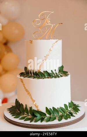 Elégant gâteau de mariage à deux niveaux avec des accents dorés et de la verdure. Banque D'Images