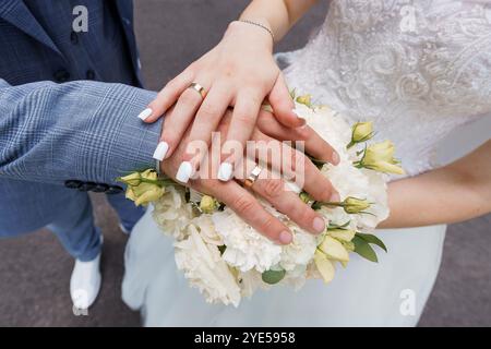 Une belle unité : mains d'un couple Newlywed affichant des bandes de mariage et un bouquet floral. Banque D'Images