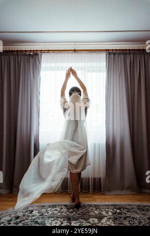 Mariée se préparant pour son jour de mariage avec Veil coulant dans la lumière douce. Banque D'Images