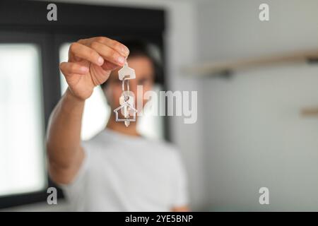 Homme souriant montrant les clés de la maison dans une pièce lumineuse, indiquant une nouvelle propriété. Banque D'Images