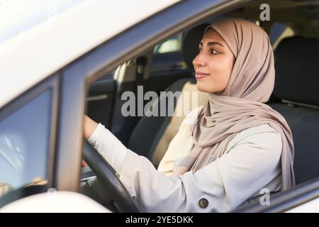 Une femme portant un hijab conduit une voiture. Elle est souriante et elle profite de sa balade Banque D'Images