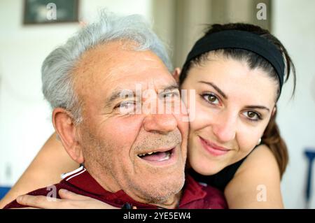 Grand-père embrassé avec sa petite-fille souriant et regardant la caméra sur la terrasse de sa maison Banque D'Images