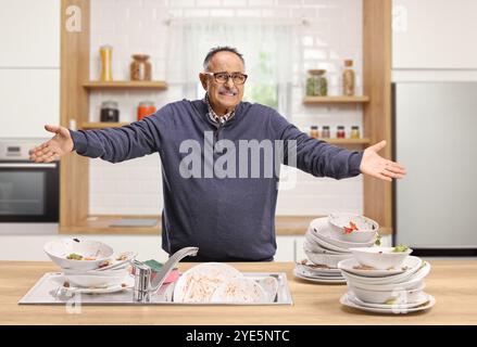 Homme mature en colère avec un tas de vaisselle sale dans la cuisine Banque D'Images