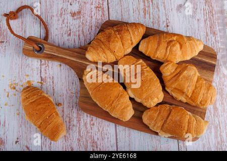 Les croissants frais reposent sur une planche à découper en bois, placée sur une table en bois clair. La vue aérienne souligne les pâtisseries chaudes et dorées dans un at rustique Banque D'Images