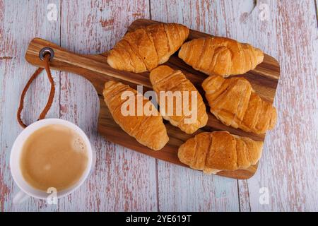 Prise de vue aérienne de croissants et de café reposant sur une planche à découper en bois, placée sur une table en bois clair, capturant une ambiance matinale détendue Banque D'Images