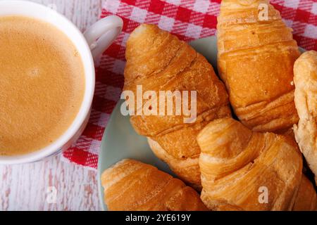 Croissants et café sont assis sur une table en bois clair, vue d'en haut. La scène accueillante du petit déjeuner apporte chaleur et confort à tout matin Banque D'Images