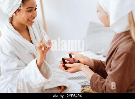 Une jeune fille noire gaie dans un peignoir en choisissant la couleur de la polisseuse des ongles Banque D'Images