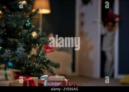 Gros plan de détail de sapin de Noël décoré avec lumière scintillante et ornement de Noël rouge de cheval jouet suspendu sur l'espace de copie de branche Banque D'Images